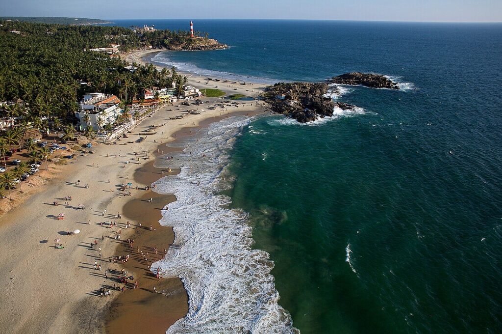 Panoramic sea view of Kovalam Beach in Kerala with the Arabian Sea, golden coastline, coconut palms and iconic Vizhinjam Lighthouse.