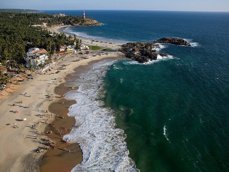 Panoramic sea view of Kovalam Beach in Kerala with the Arabian Sea, golden coastline, coconut palms and iconic Vizhinjam Lighthouse.